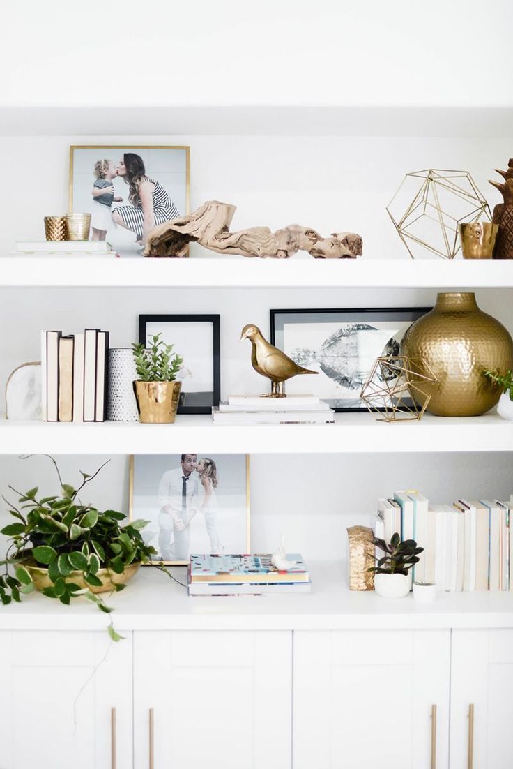 white shelves with gold vases, books and pictures on them in a living room