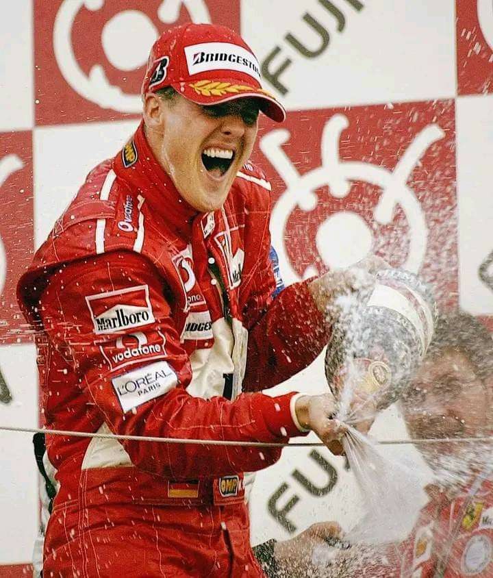 a man in a red racing suit is spraying water on his face and hands as he celebrates