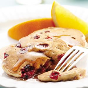 a white plate topped with pancakes covered in icing next to an orange wedge and a fork