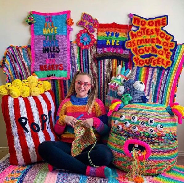 a woman sitting on the floor next to some knitted items