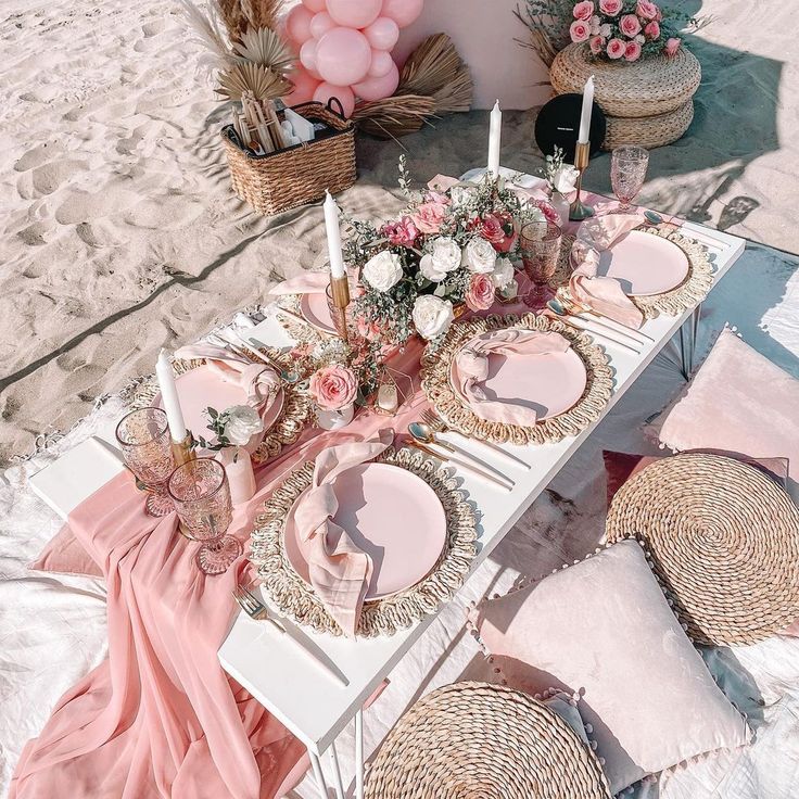 a table set up with pink plates and place settings on the beach for a party