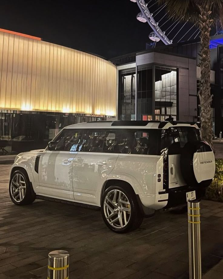 a white suv is parked in front of a building at night with its door open