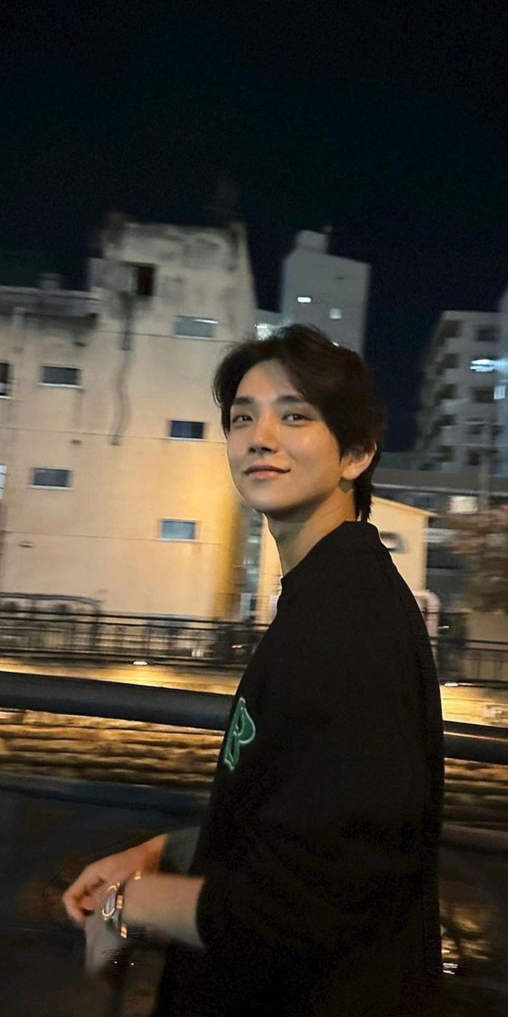 a man in black shirt walking down street next to tall buildings at night with city lights behind him