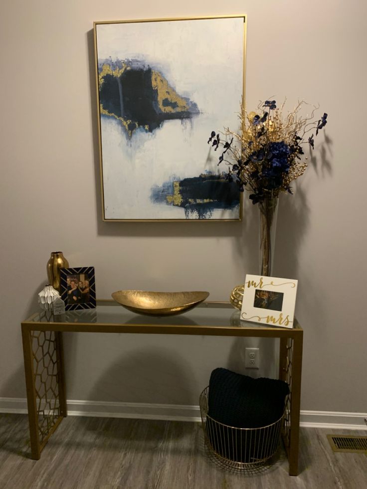 a vase with flowers on top of a table next to a gold plate and framed painting