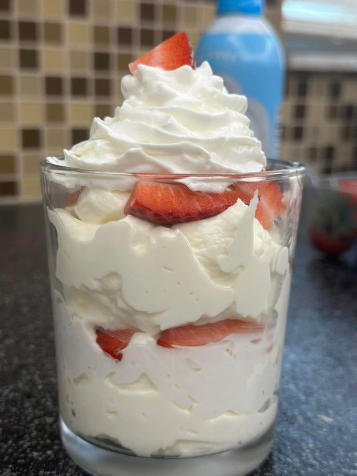 a dessert with whipped cream and strawberries in a glass on a counter top next to a bottle of water