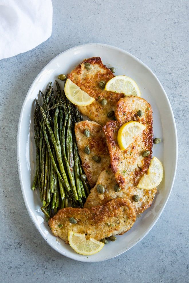 a white plate topped with chicken, asparagus and lemon slices