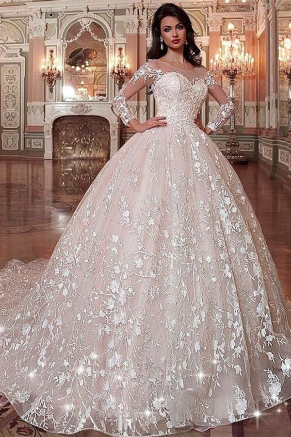 a woman in a wedding dress with white flowers on the skirt and long sleeves, posing for