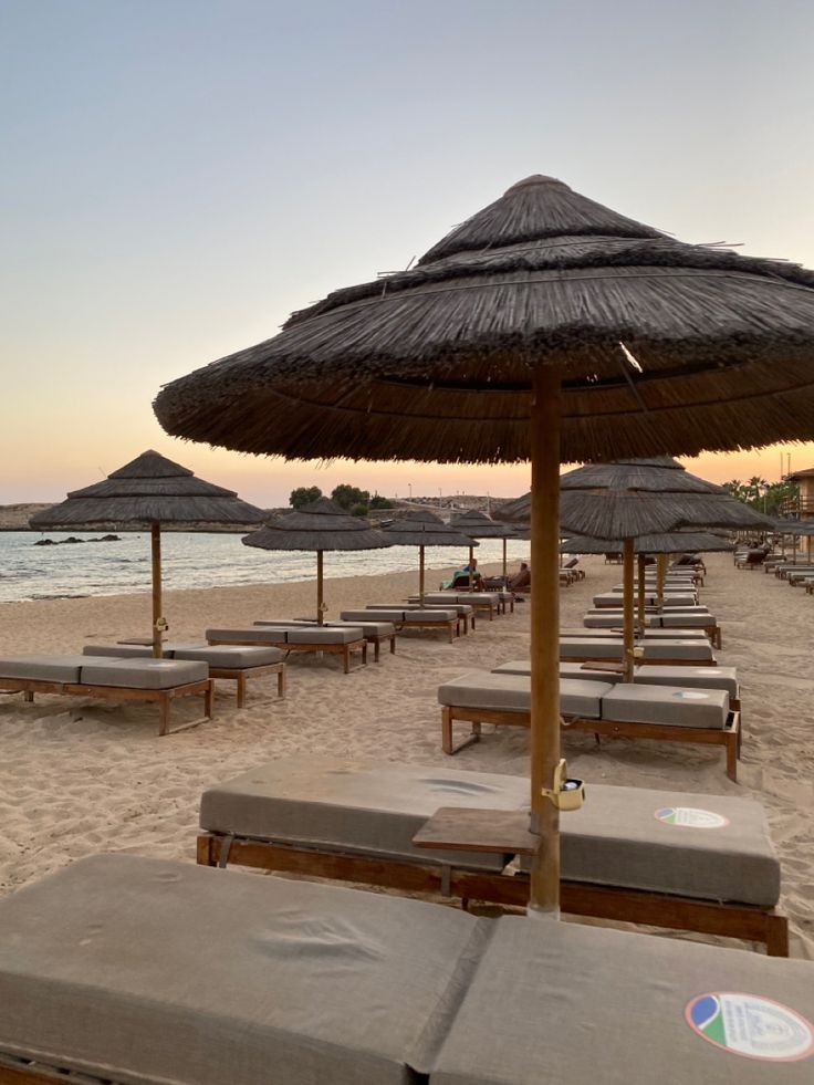 lounge chairs and umbrellas on the beach at sunset