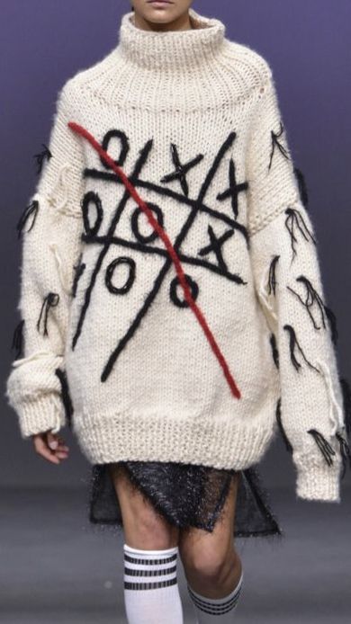 a model walks down the runway in a white sweater with black and red letters on it