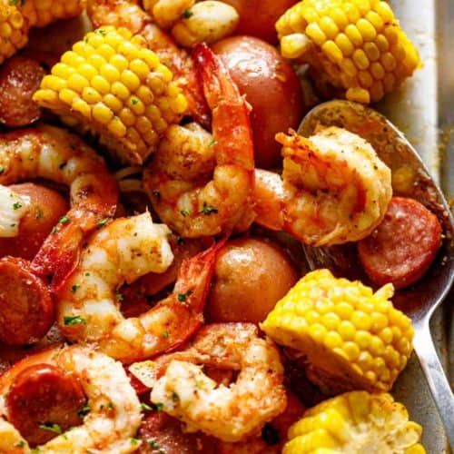 shrimp, corn on the cob and potatoes in a skillet with a spoon