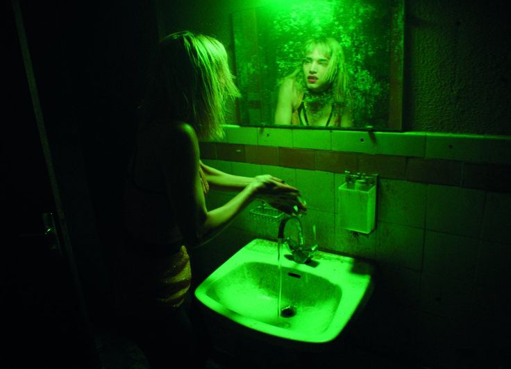 a woman standing in front of a bathroom mirror with green light shining on her face