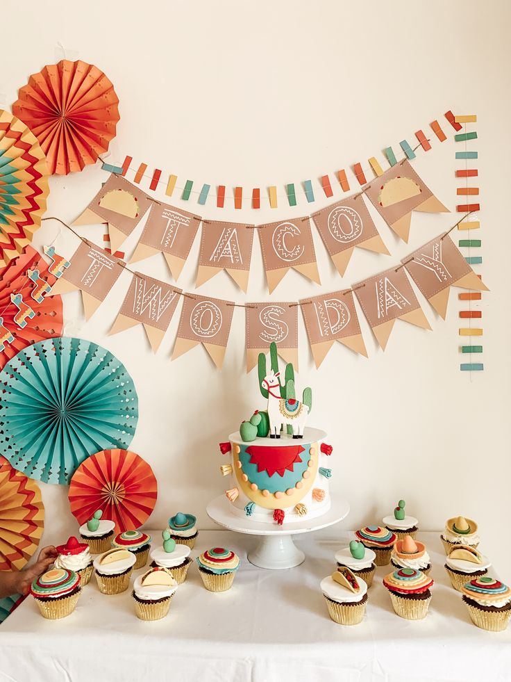 a table topped with cupcakes and cakes covered in frosting next to paper fans