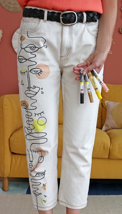 a woman is standing in front of a yellow couch holding four pens and pencils