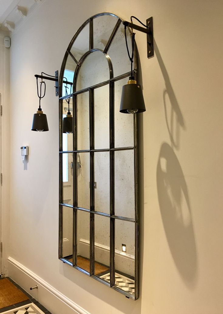 an arched mirror hanging on the wall next to a light fixture and floor lamp in a room