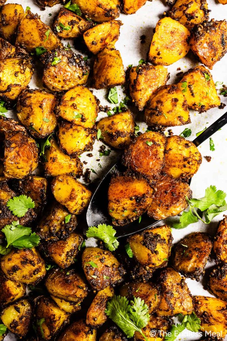 roasted potatoes with cilantro and parsley on a white plate next to a serving spoon