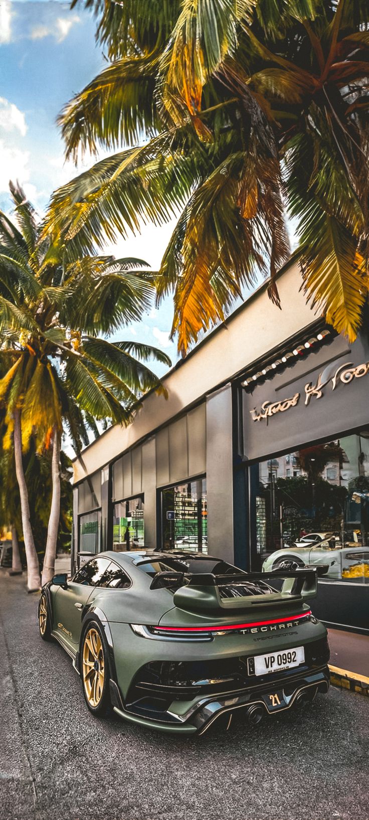 two sports cars parked in front of a building with palm trees on the side walk