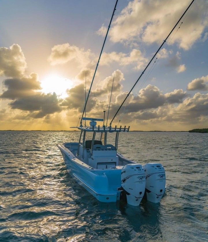 a white boat in the middle of the ocean with clouds and sun shining behind it