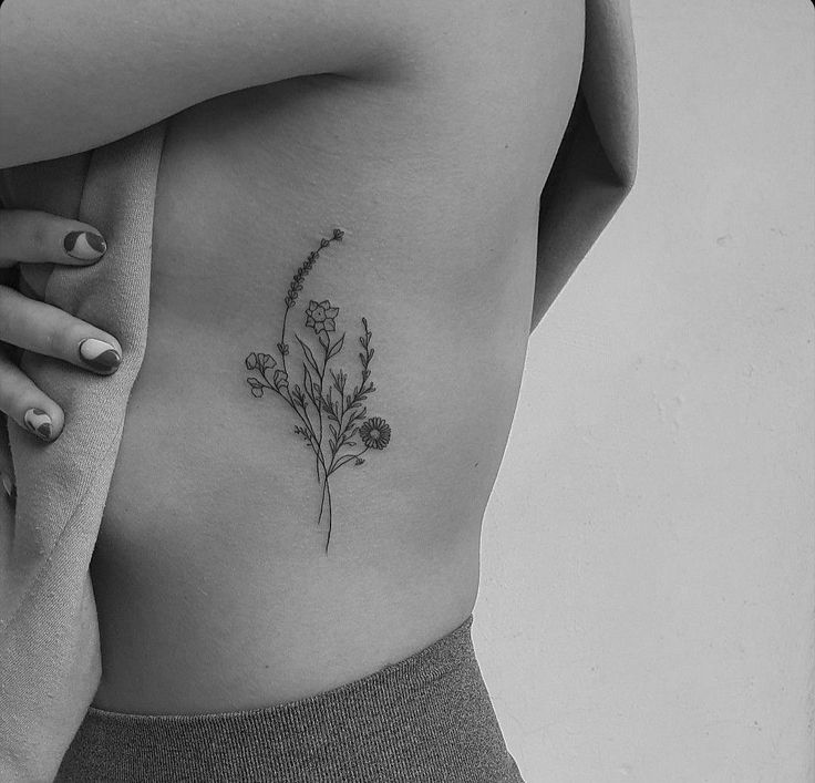 a woman's back with a flower tattoo on her left side ribcage