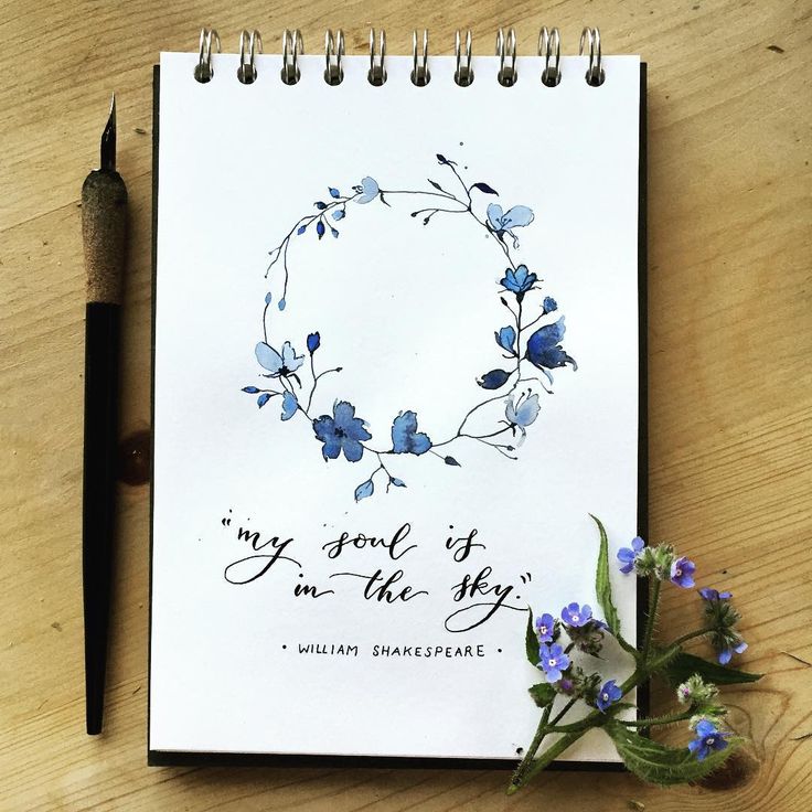 a notepad with blue flowers and a pen sitting on a wooden table next to it