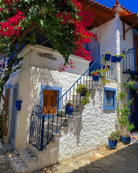 a white house with blue trim and flowers on the outside wall, stairs leading up to it