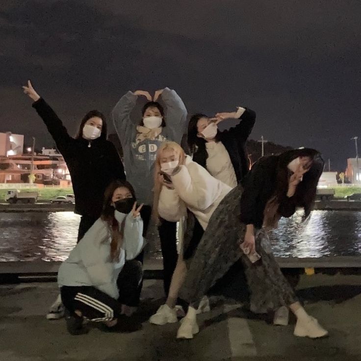 four people posing for a photo in front of the water with their hands up and one person wearing a face mask