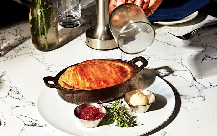 a white plate topped with food on top of a marble table next to glasses and utensils