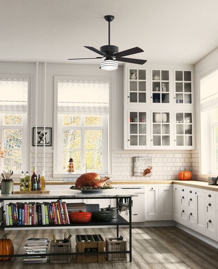 a kitchen with white cabinets and lots of books on the counter top, along with a ceiling fan