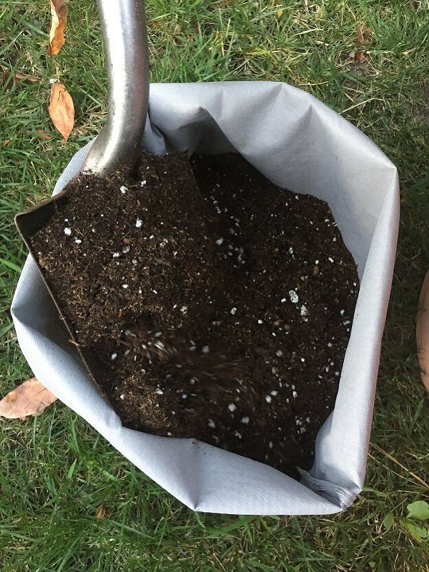 a shovel is digging dirt into the soil in a bag on the grass with leaves