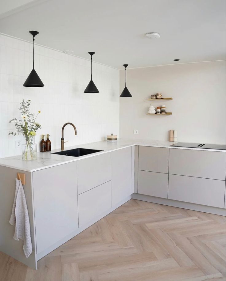 a kitchen with white cabinets and black pendant lights hanging from the ceiling over the sink