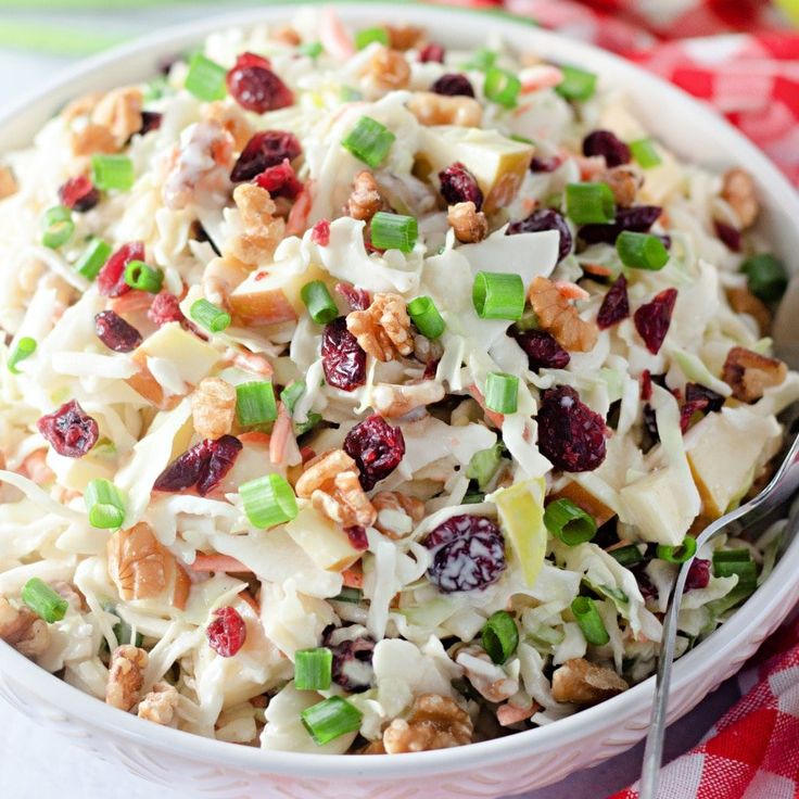 a white bowl filled with coleslaw, nuts and cranberries on top of a checkered table cloth