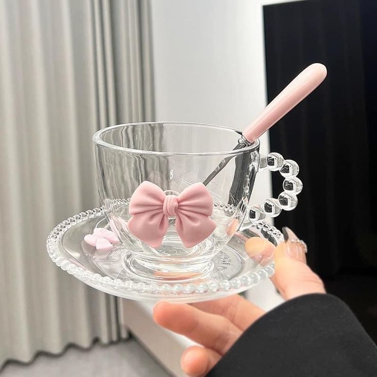 a person holding a glass cup with a pink bow on it and a spoon in the middle