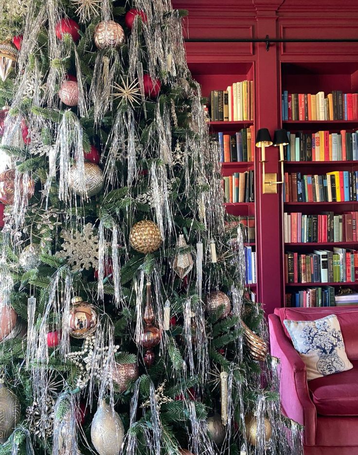 a decorated christmas tree in front of a red couch and bookshelf filled with books