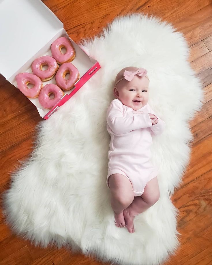 a baby is laying on a white rug with doughnuts in front of it