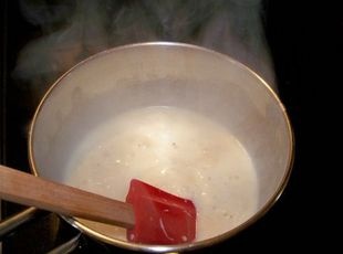 a pan with some food cooking in it on top of the stove, next to a wooden spatula