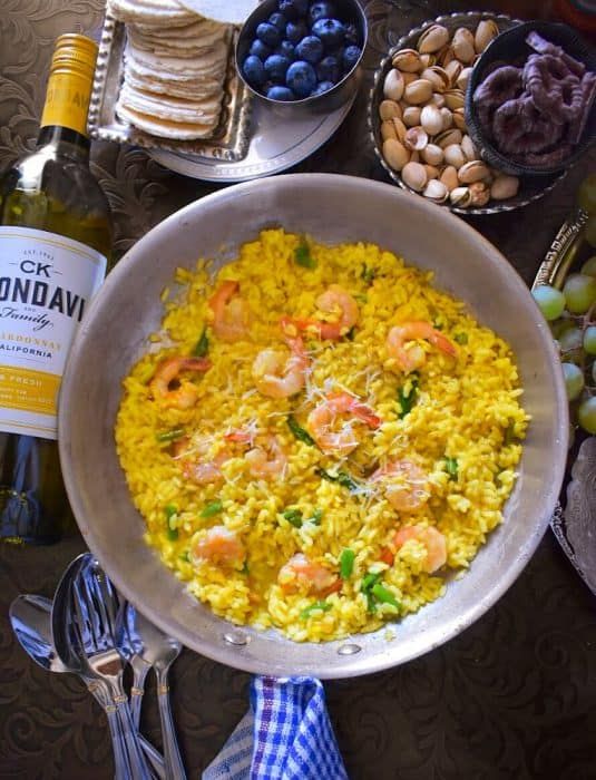 a bowl filled with rice and shrimp next to other food on a table, along with two bottles of wine