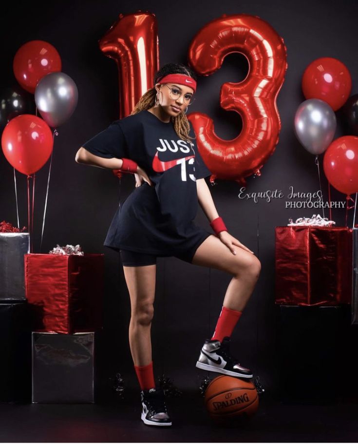 a woman posing for a photo with balloons and presents in front of the number thirteen