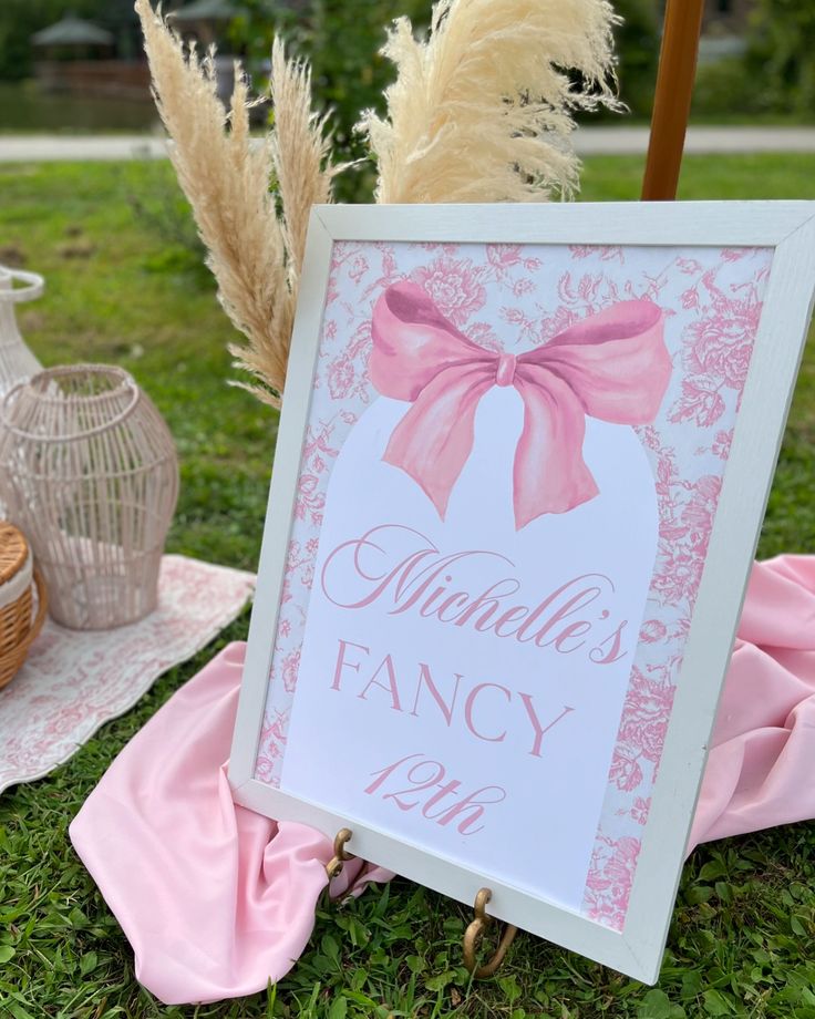 a pink and white sign sitting on top of a grass covered field next to flowers