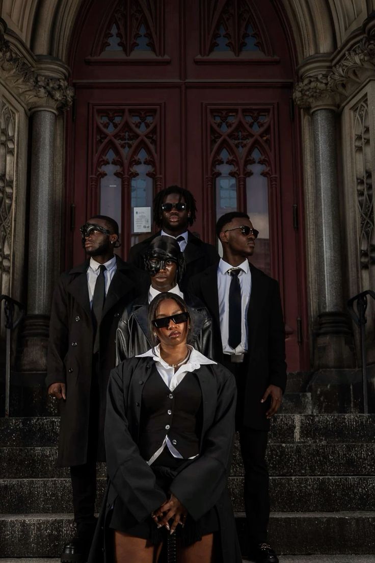 a group of people standing in front of a red door wearing black clothes and sunglasses