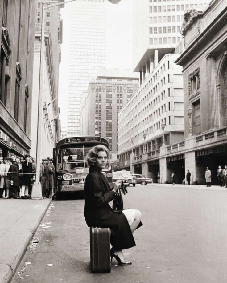 a woman sitting on top of a suitcase in the middle of an empty city street