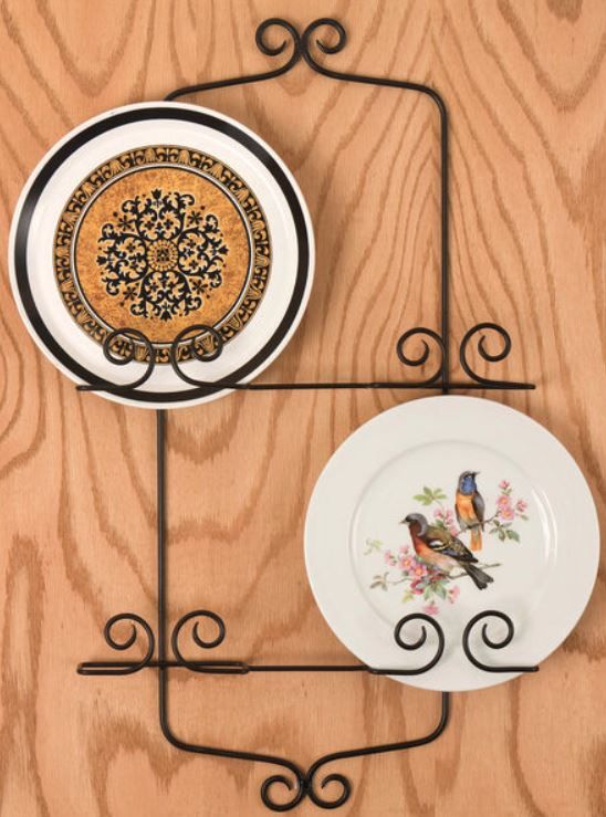 two plates are hanging on the wall with wrought iron racks holding them and one has a bird plate in it