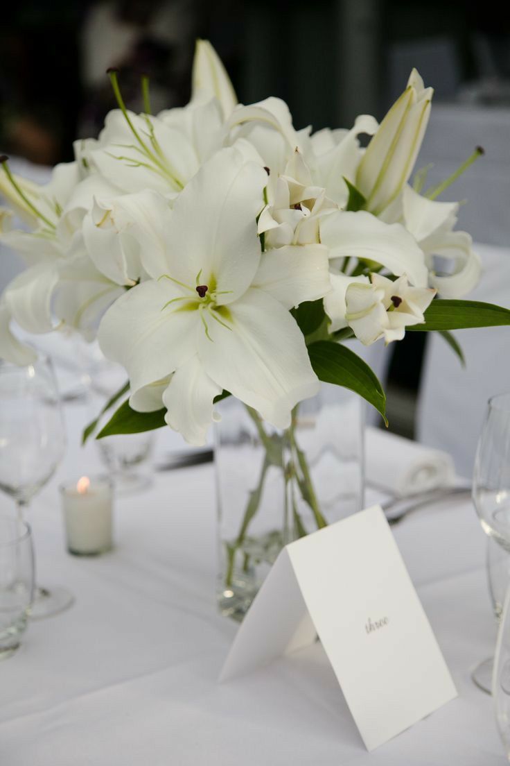 a vase filled with white flowers sitting on top of a table next to wine glasses