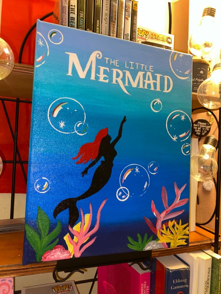 the little mermaid book is on display in front of bookshelves and other items