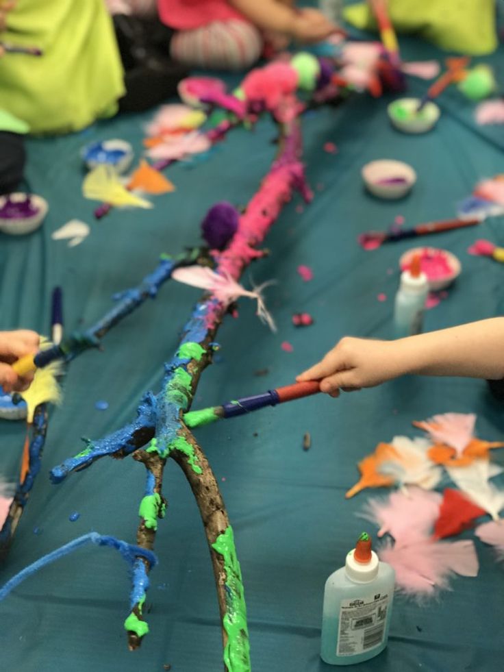 two children are painting on a table with paintbrushes and other craft supplies in the background