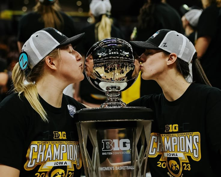 two women kissing each other in front of a trophy with their faces covered by caps