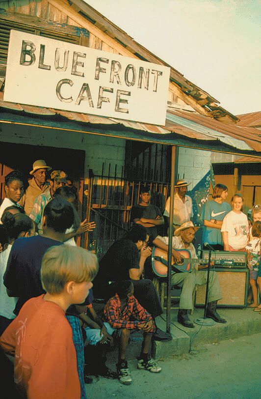 a group of people sitting outside of a blue front cafe