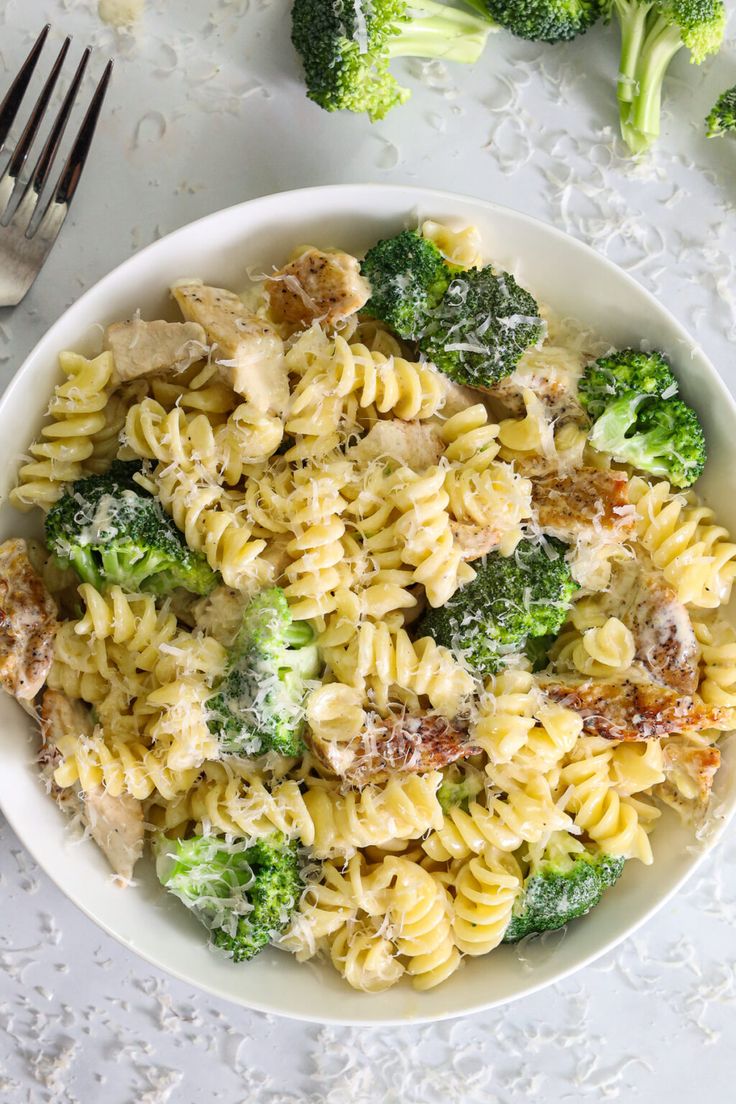 a white bowl filled with pasta and broccoli on top of a table next to silverware