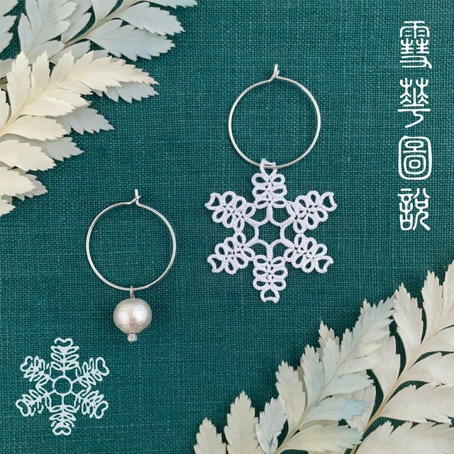 two silver hoop earrings with snowflakes and pearls on them next to some leaves