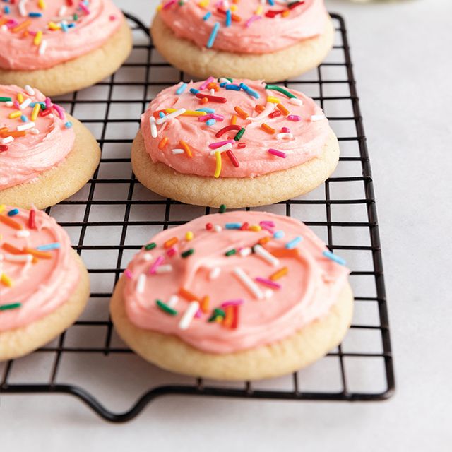 several cookies with pink frosting and sprinkles on a cooling rack