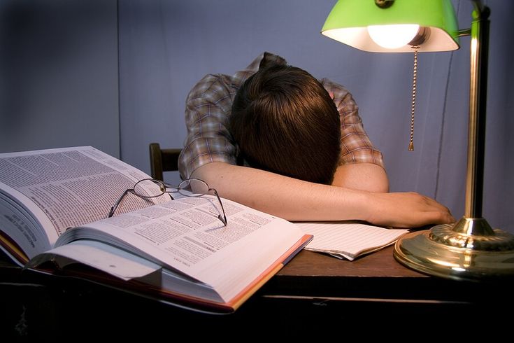 a person is asleep on a desk with an open book and a lamp in front of them