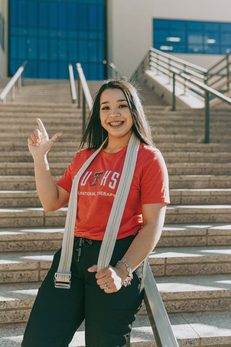 a woman standing in front of some stairs with her hand up and smiling at the camera